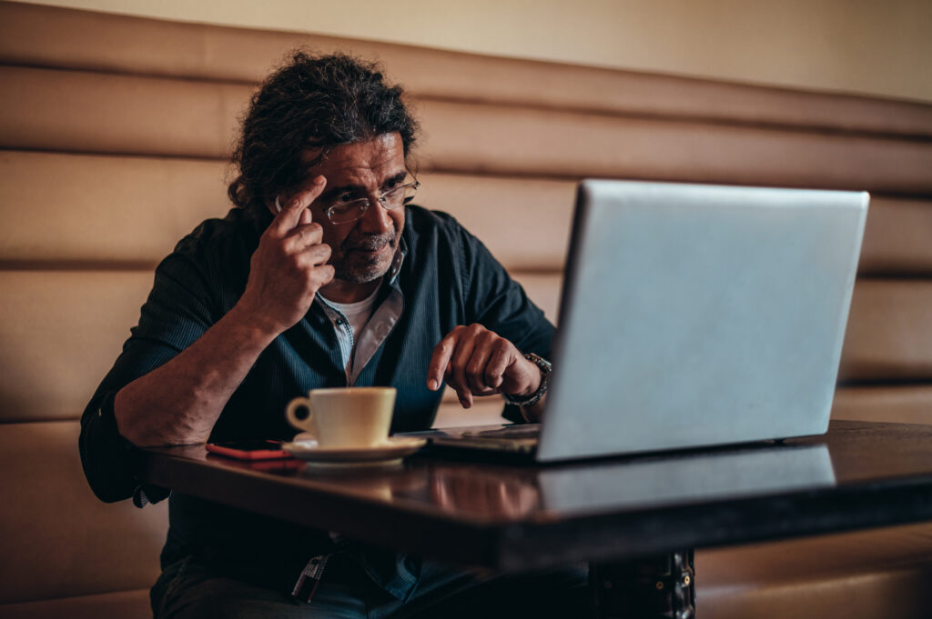 Senior hispanic cuban men using laptop while working remotely in a cafe